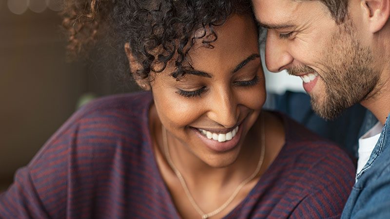 A man and a woman smiling while leaning their heads against one another