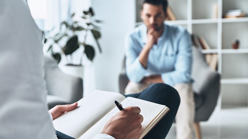 A person writing in a notebook while another is looking at them